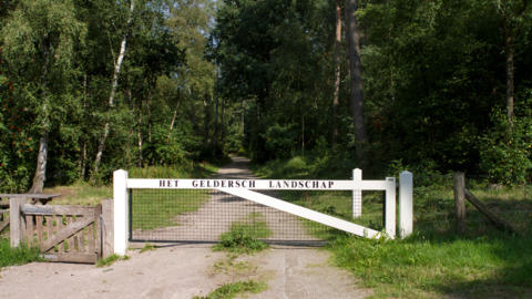 Wit hek bij een bos met de tekst "Het Geldersch Landschap"